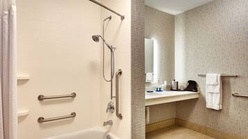 A bathroom with a bathtub, a shower with grab bars, a sink with a mirror, and a towel rack.
