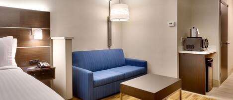 Habitación de hotel con una cama, un sofá azul, una mesita, una lámpara, microondas y un armario.
