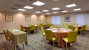 A conference room with multiple tables and chairs, equipped with water bottles and papers, and a projector screen on the wall.