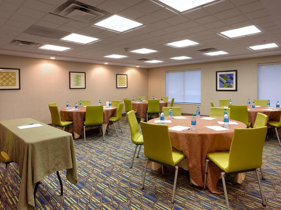 A conference room with multiple tables and chairs, equipped with water bottles and papers, and a projector screen on the wall.