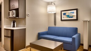 Un espacio habitable compacto con kitchenette, un sofá azul, una mesita y un cuadro abstracto enmarcado en la pared.