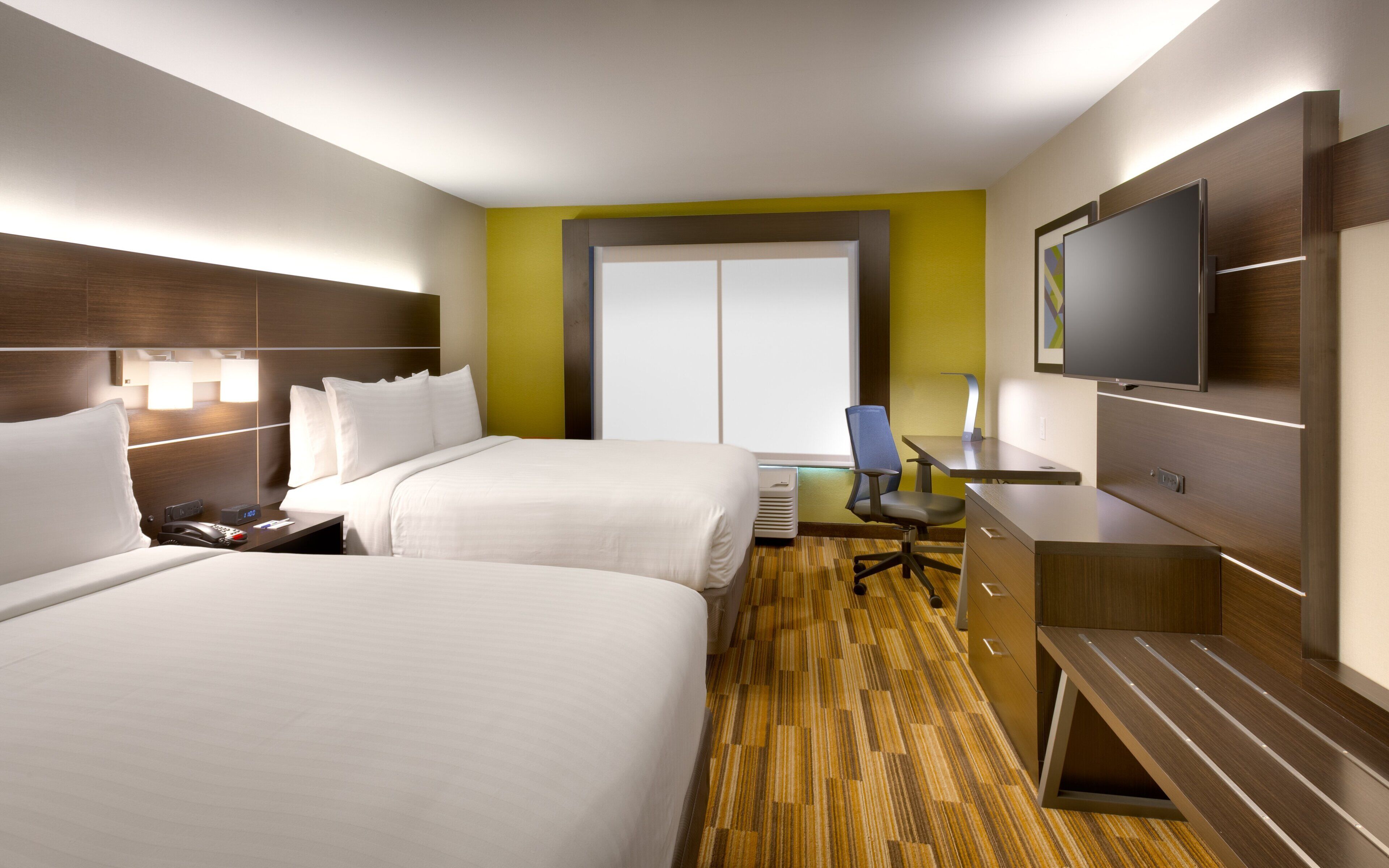 Habitación de hotel con dos camas, un escritorio, una silla, un televisor y un ventanal grande.