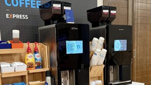 Een koffiehoek met meerdere koffieautomaten, voorzien van de aanduiding 'Costa Coffee', en een bord waarop staat 'MUST. HAVE. COFFEE EXPRESS'. Ook zijn er koffiecups, een koffiezetapparaat en een presentatie van wegwerpbekers.