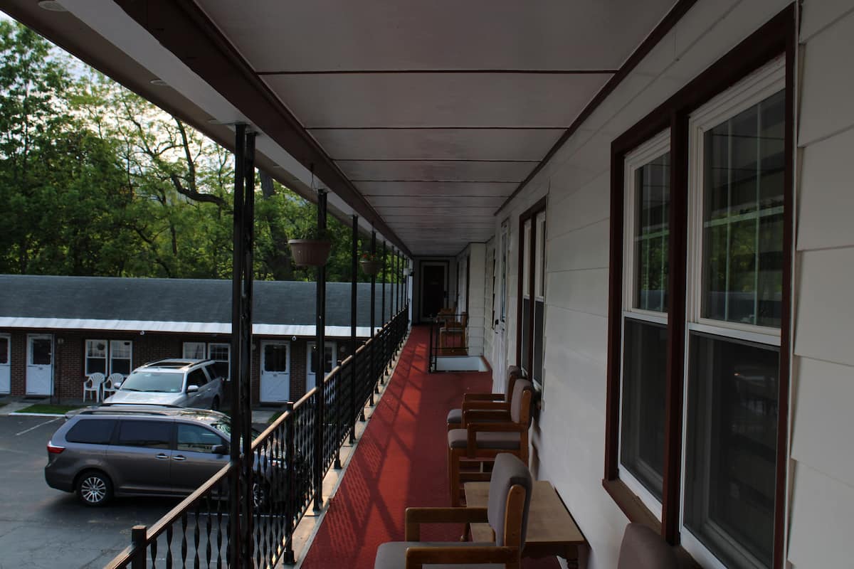 A covered corridor with a red carpet, wooden benches, and hanging planters.