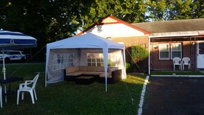 A tent with a cushioned seating area, a table, and chairs outside a building with a brick facade. - Northside Motel (Williamstown)