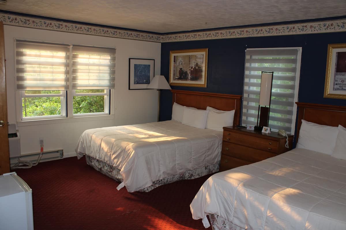 A bedroom with two beds, a dresser, a mirror, and a window with blinds.