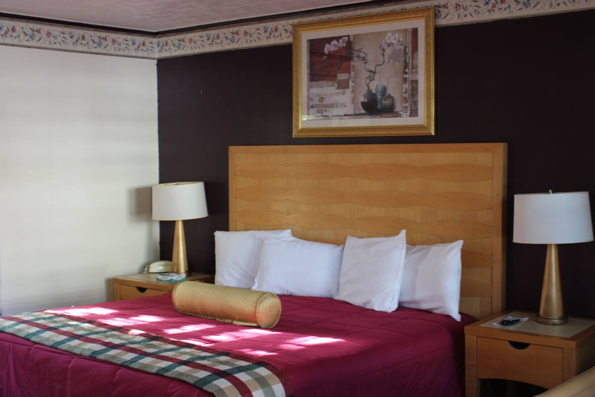 A hotel room with a large bed, two bedside tables with lamps, a wooden headboard, and a framed picture on the wall.