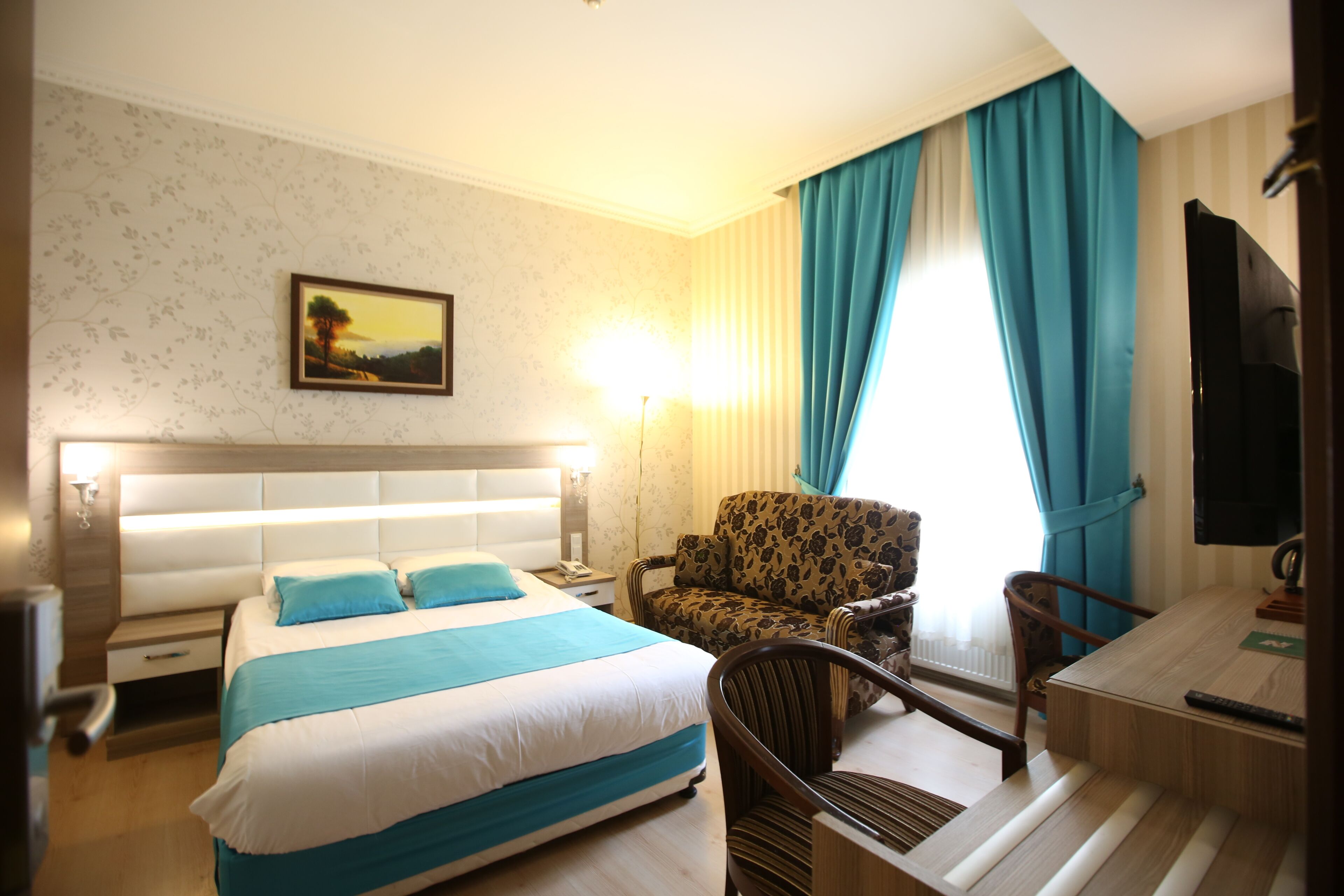 Una habitación de hotel con cama, una silla, un escritorio, un televisor y un cuadro en la pared.
