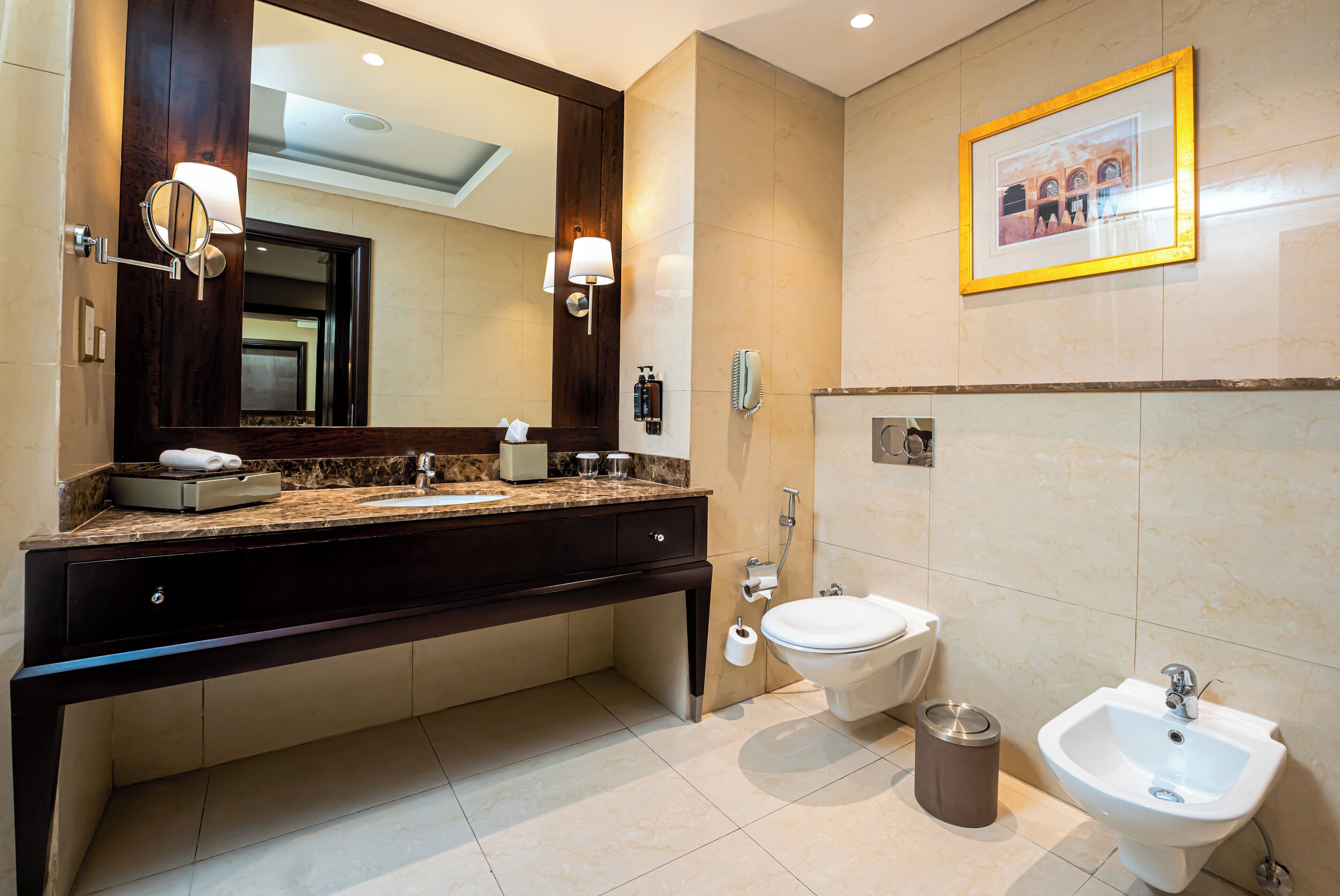 A modern bathroom with a dark wood vanity, a large mirror, a toilet, a bidet, and a sink.