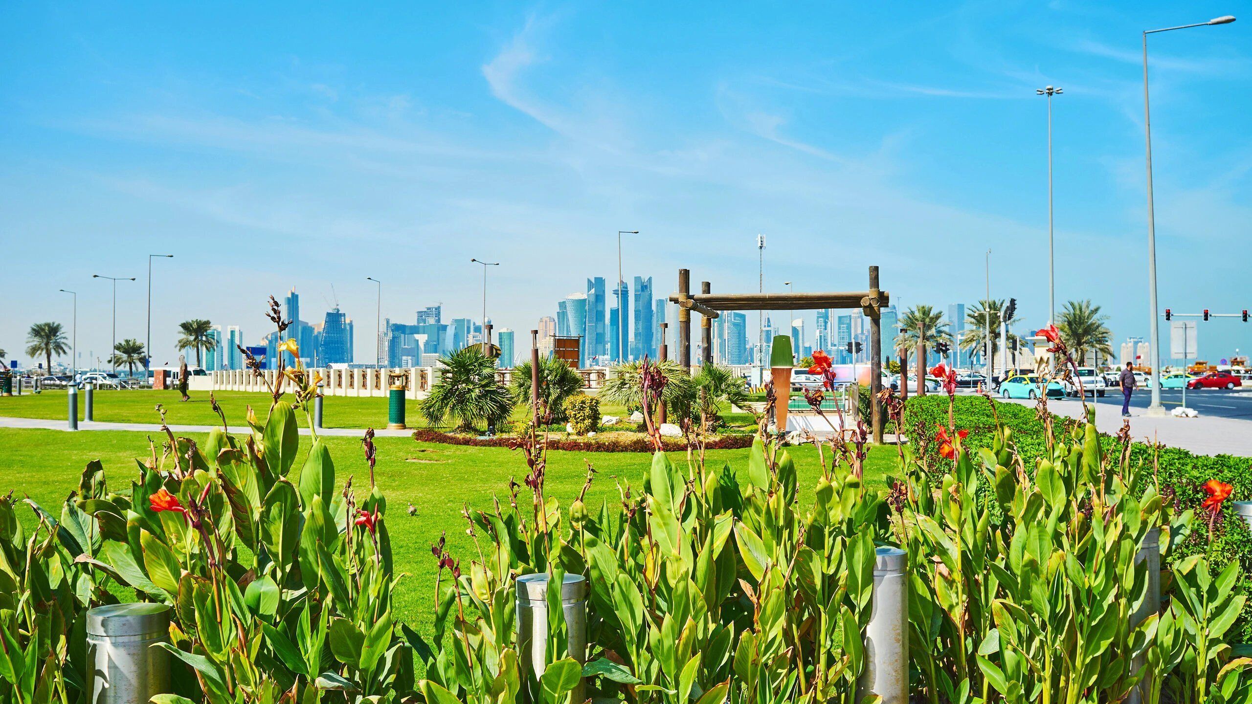 A park with a metal sculpture, green grass, and a city skyline in the background.