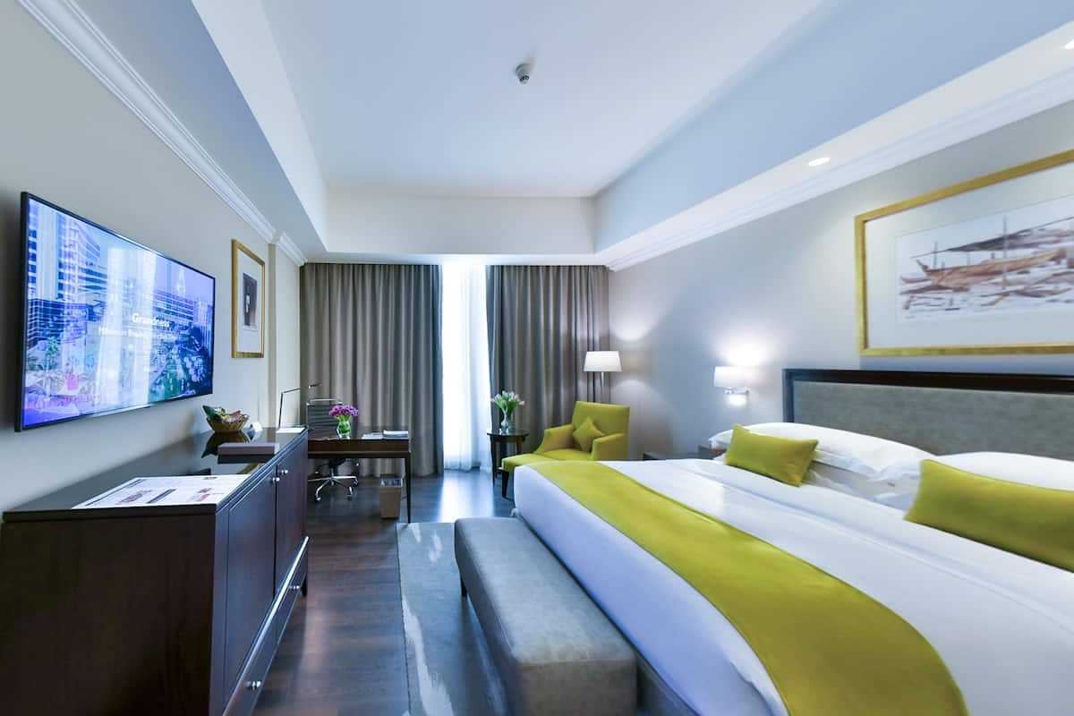 A hotel room with a large bed, a desk, a chair, a television, and a window with curtains.