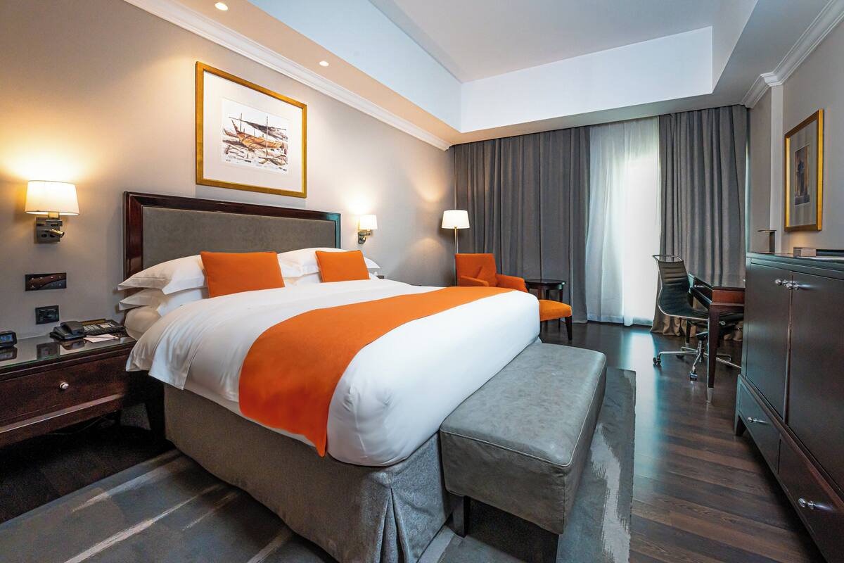 A hotel room with a large bed, two bedside tables, a desk, a chair, and a wardrobe.