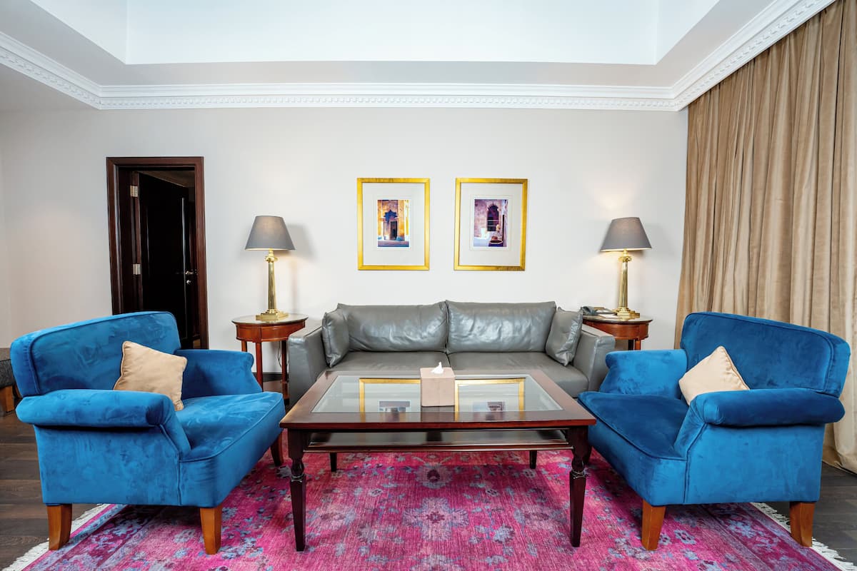 A living room with a glass coffee table, two blue armchairs, a grey sofa, and two lamps.