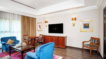 Una sala de estar moderna con un televisor de pantalla plana grande, sillones azules, una mesa de centro de madera y una alfombra roja estampada.