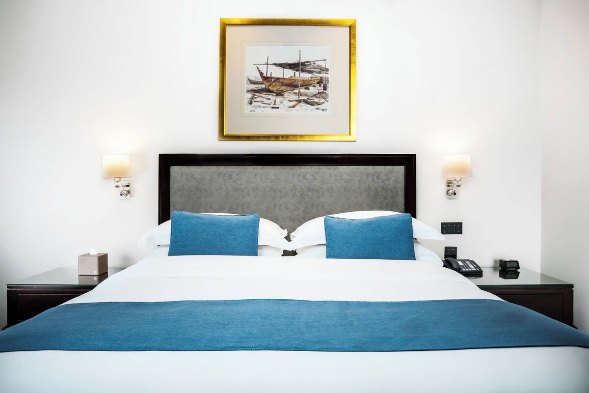 A hotel room with a large bed, two bedside tables, a framed artwork above the bed, and a nightstand with a phone and a lamp.