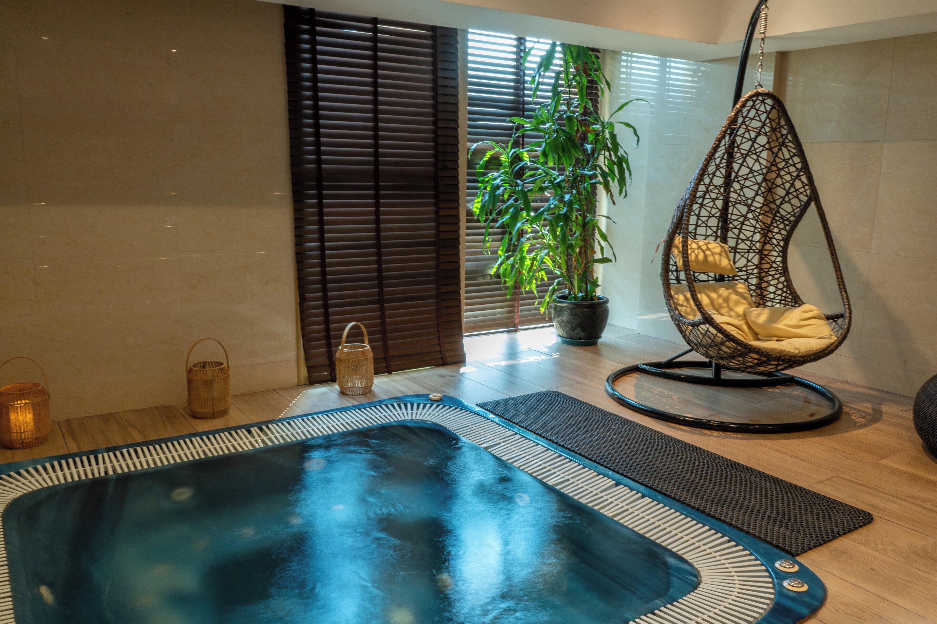 A spa area with a hot tub, a hanging chair, a potted plant, and a window with blinds.