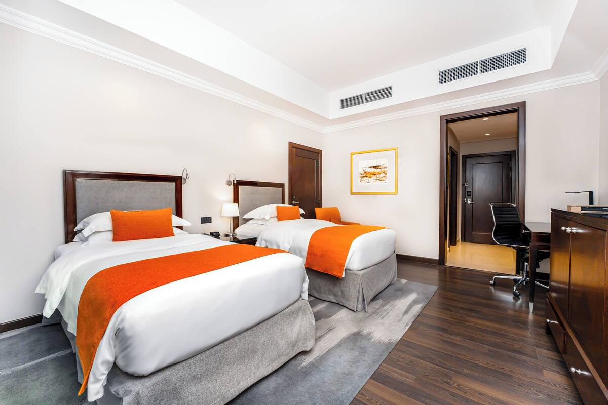 A hotel room with two beds, a desk, and a chair.