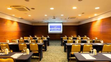 Une salle de conférence équipée de tables, de chaises et d’un écran de projection sur lequel est affiché le logo « NOVOTEL Hotels & Resorts ».