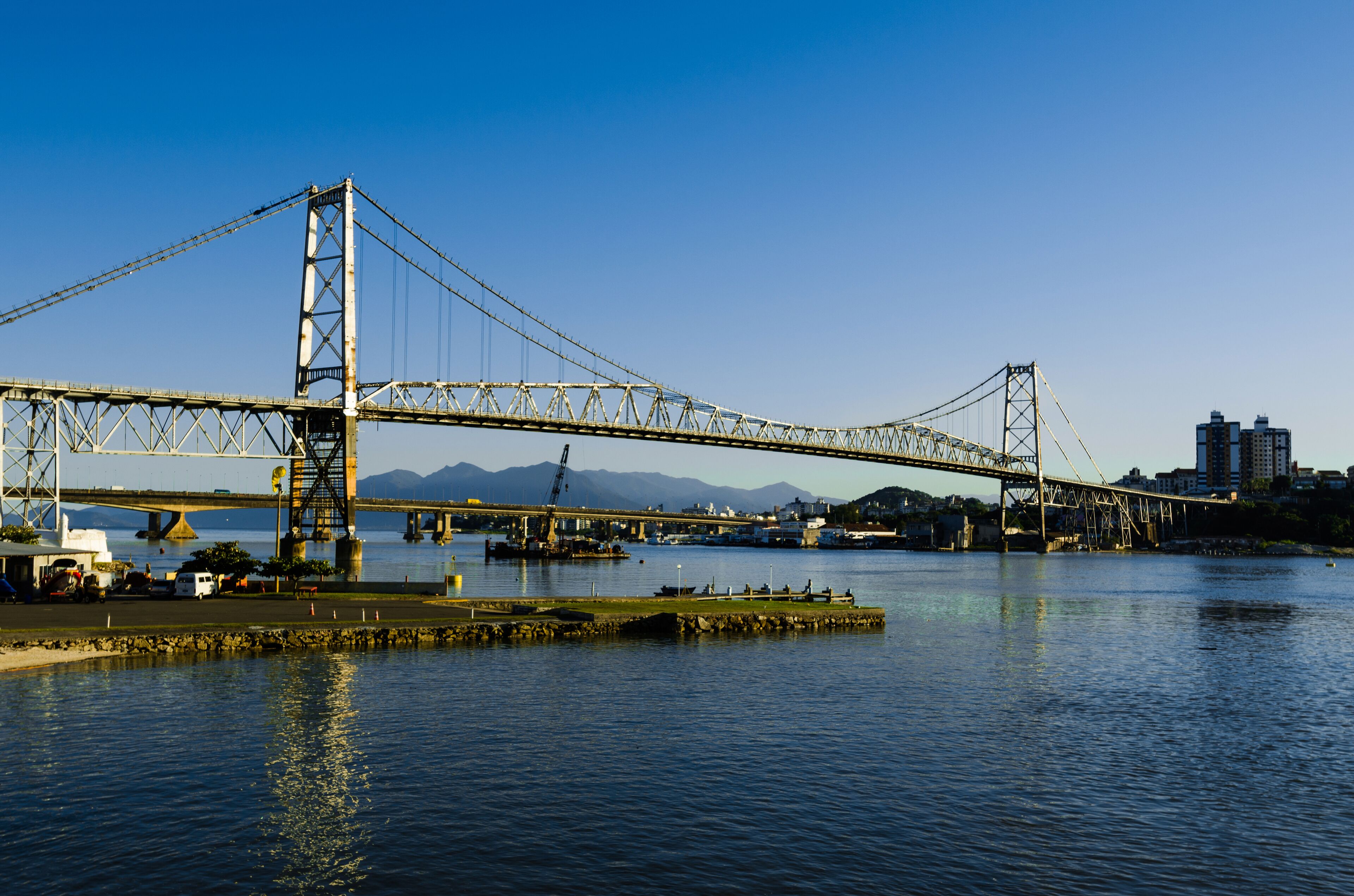 Un gran puente colgante sobre una masa de agua, con un paisaje urbano al fondo.