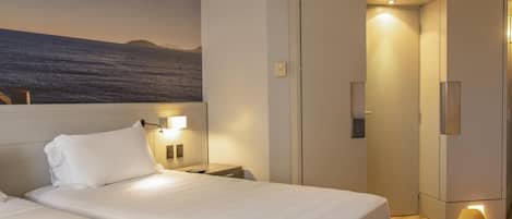 A hotel room with two beds, a nightstand, a lamp, a wardrobe, and a painting of a landscape.