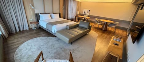 A modern hotel room with a large bed, a sofa, a desk, and a chair.