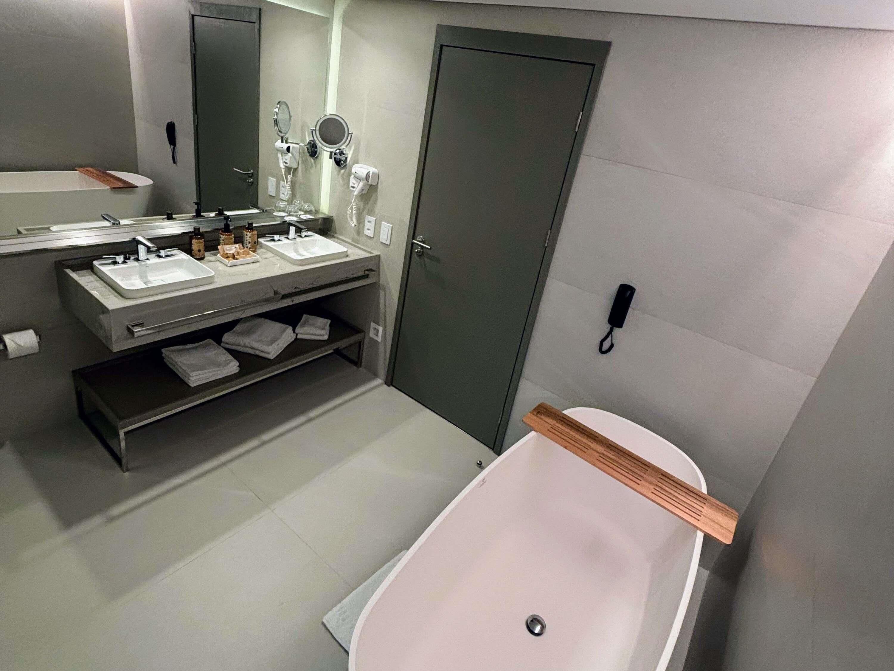 A modern bathroom with a sink, mirror, hairdryer, and a bathtub.