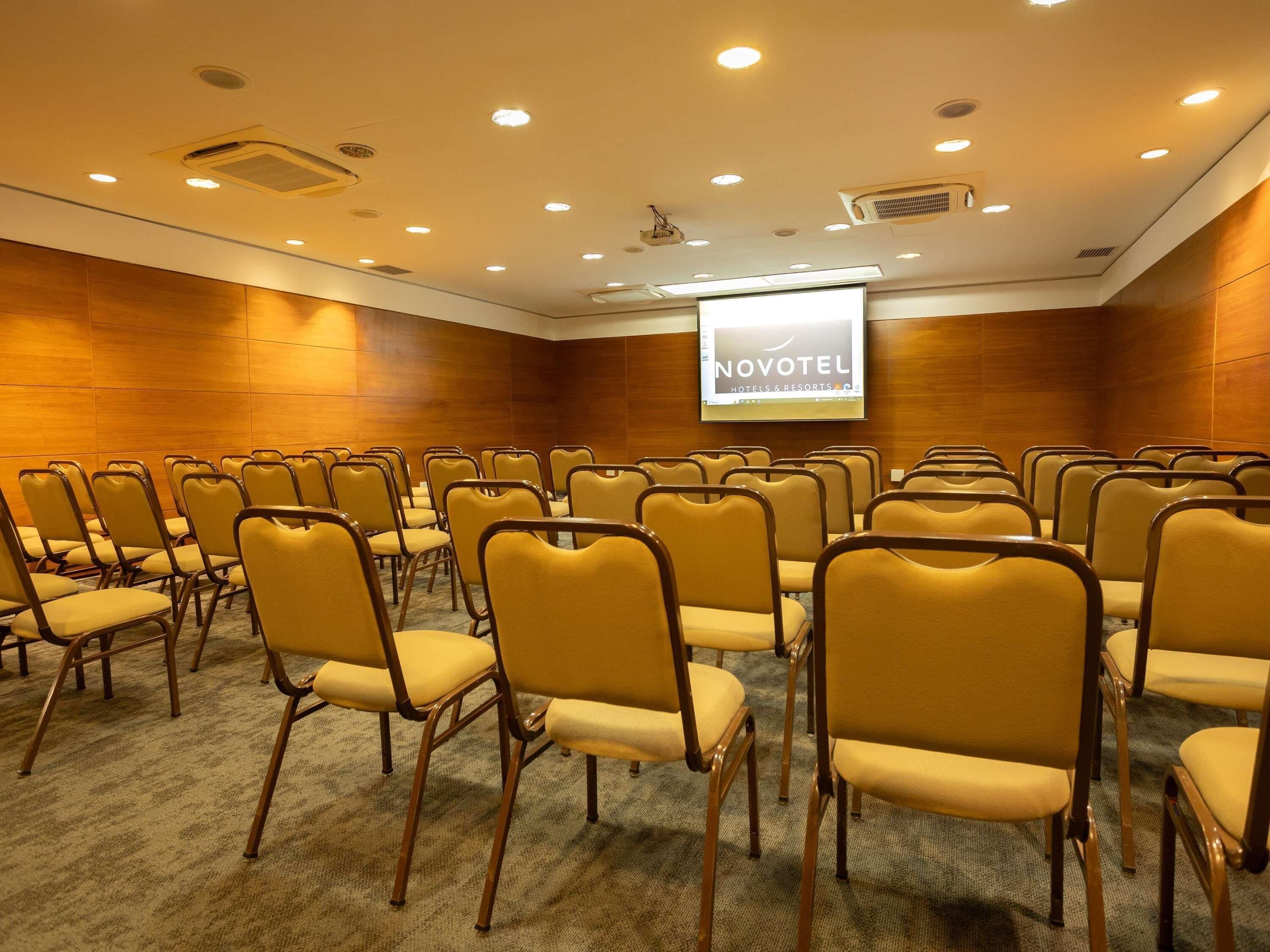 A conference room with rows of chairs, a projector screen, and a wooden wall.