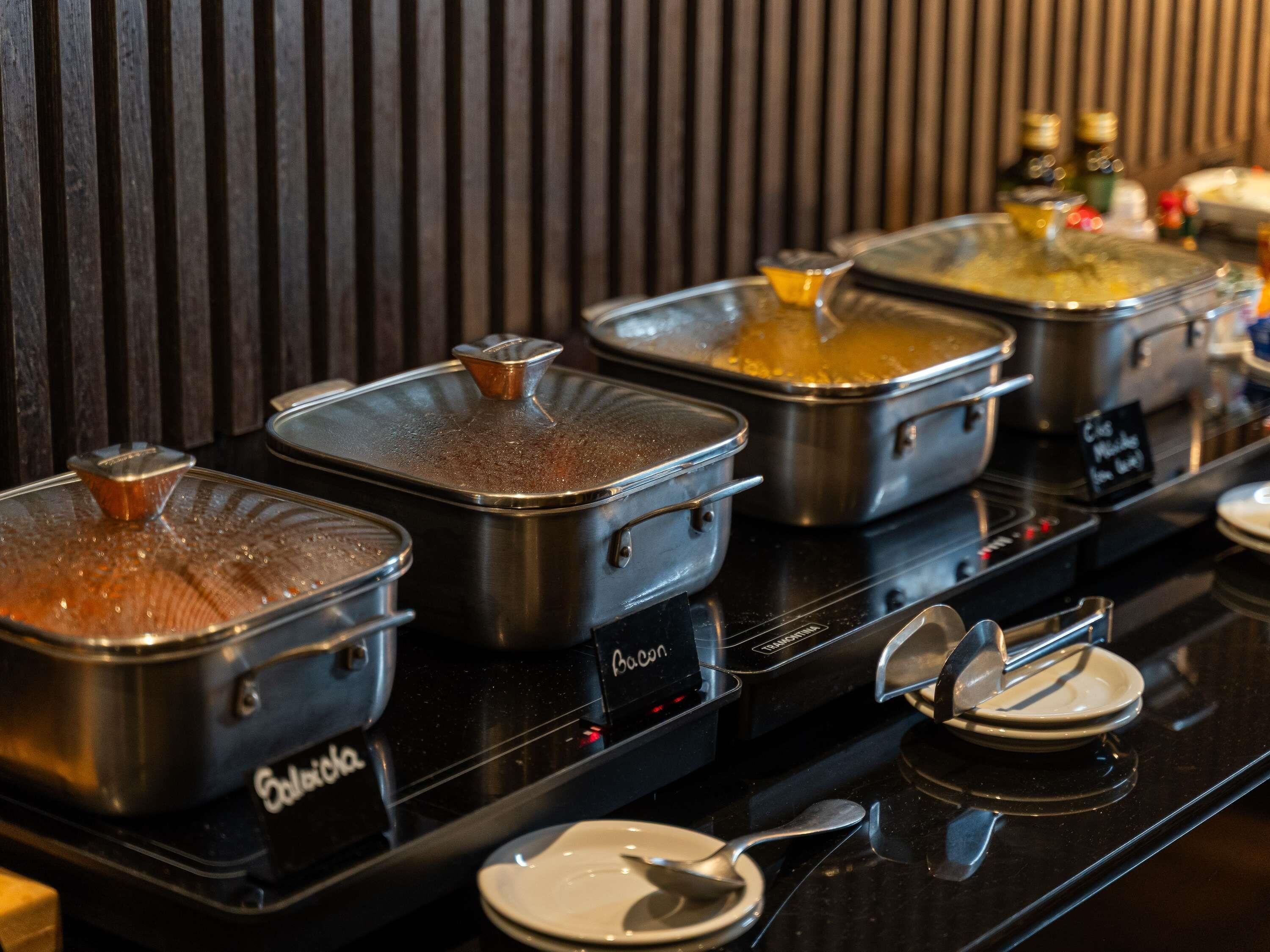 A buffet setup with multiple stainless steel chafing dishes on a black countertop, each with a lid.