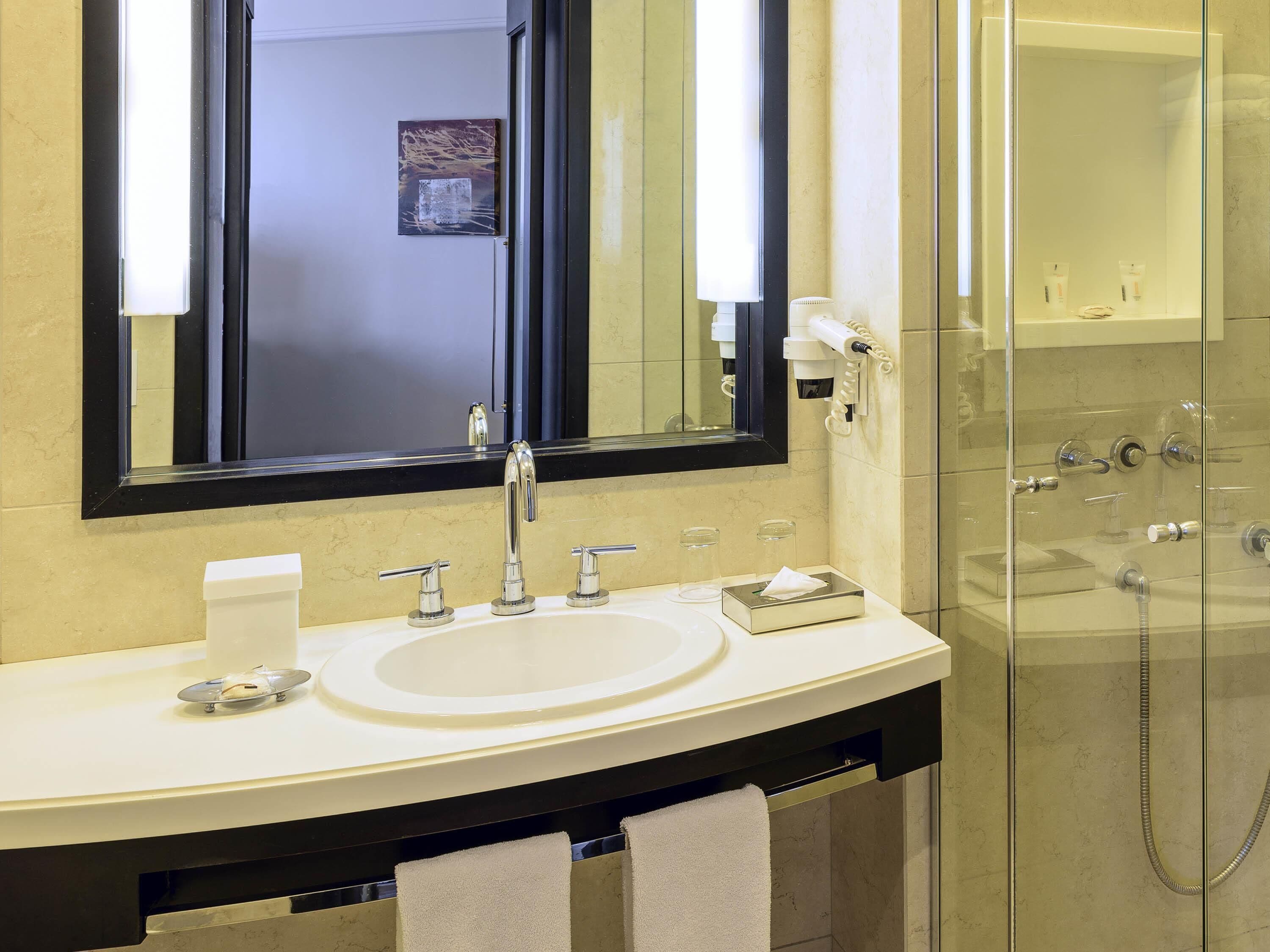 Une salle de bain dotée d’un grand miroir, d’un lavabo avec un porte-serviettes et d’une douche à parois de verre.