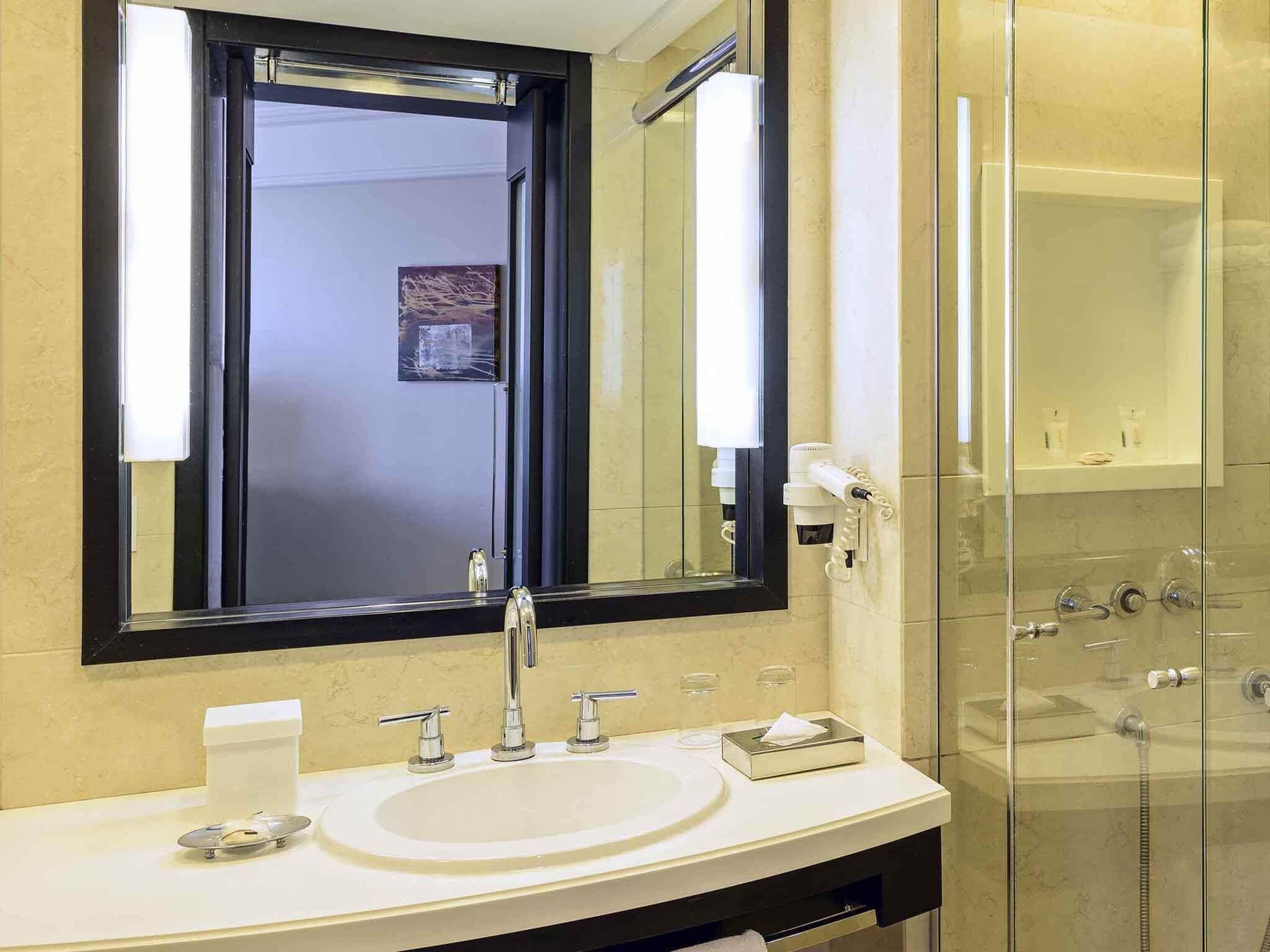 Un baño con un espejo grande, un lavabo, cabina de ducha de vidrio y un perchero para toallas.