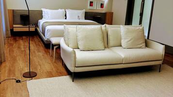 A modern hotel room with a bed, a sofa, a floor lamp, and a rug.