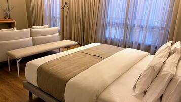 A hotel room with a large bed, a bench, a sofa, and a bedside table.