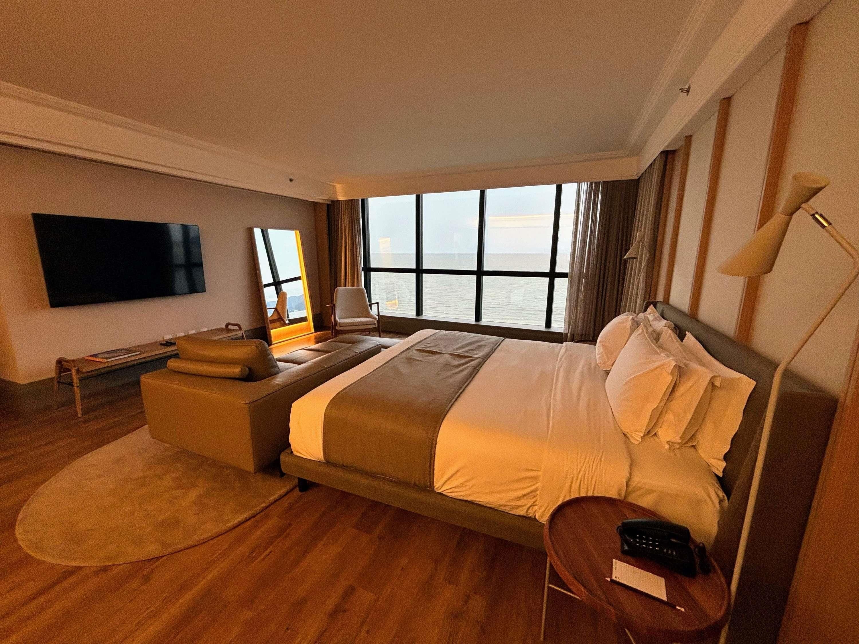Een hotelkamer met een groot bed, een televisie, een bureau en uitzicht op zee.