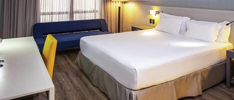 Habitación de hotel con cama, escritorio, sofá y un cuadro de playa.