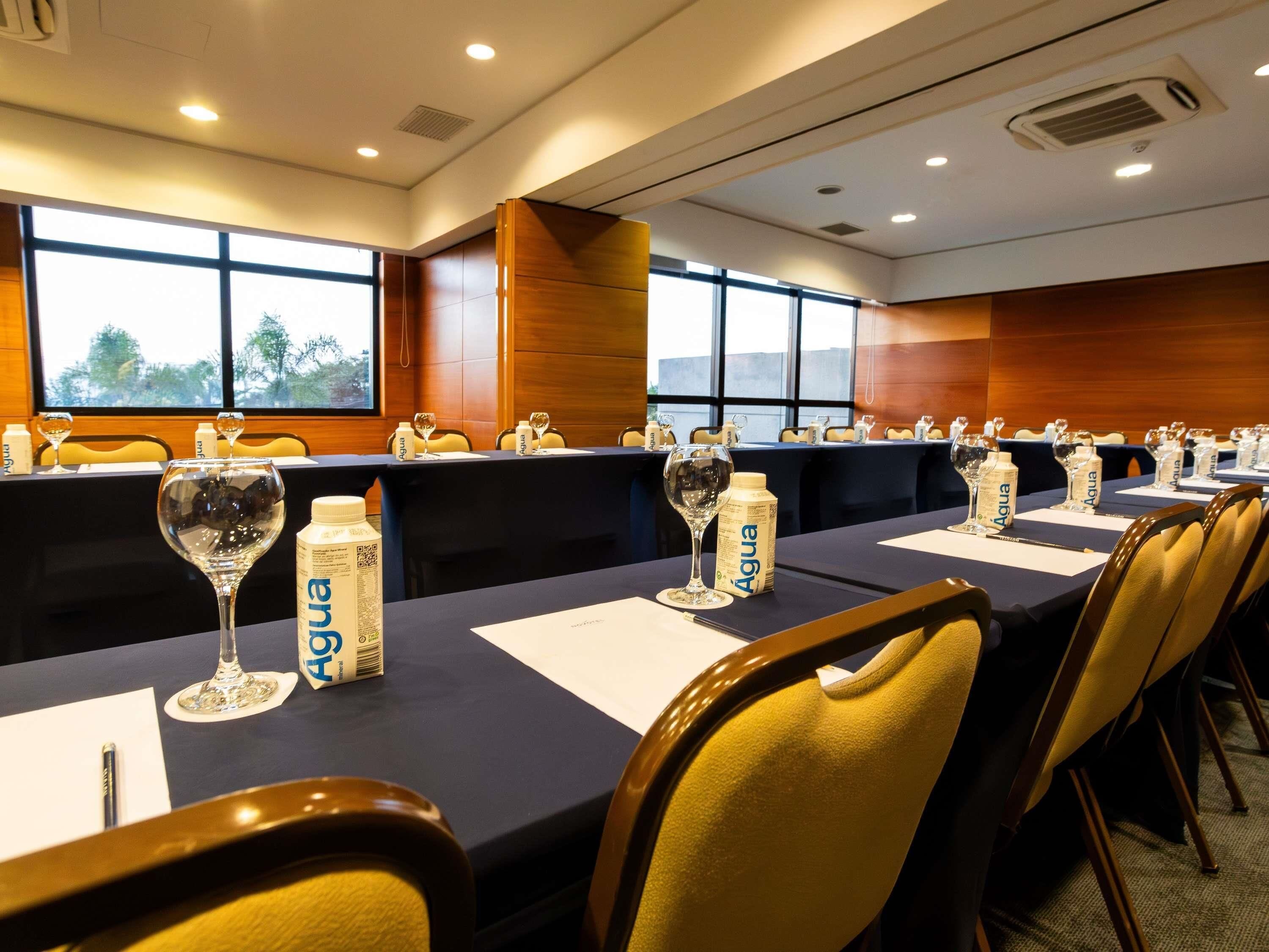 A conference room with long tables, chairs, and water bottles labeled 'Agua.'