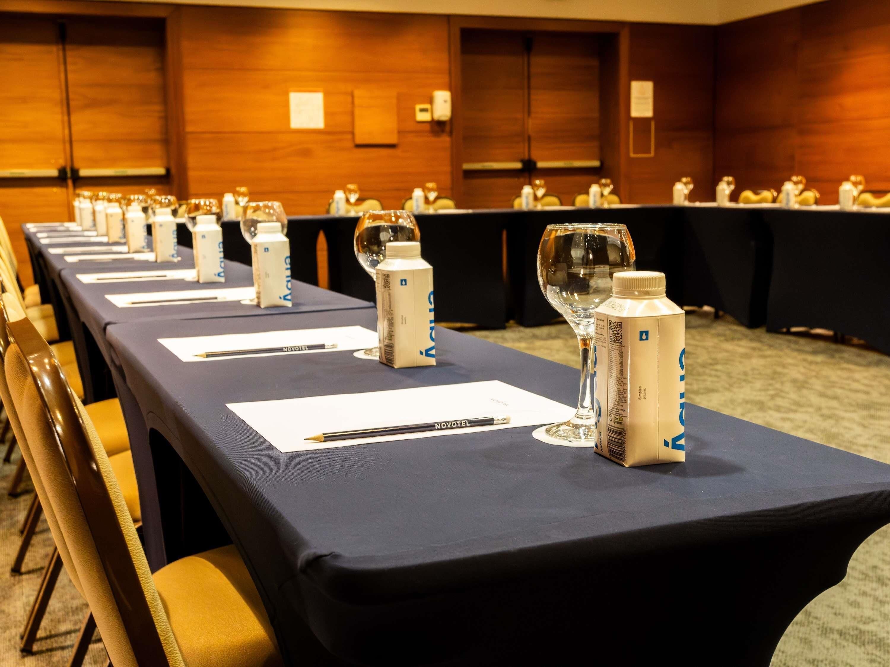 Un salón de conferencias con mesas largas, tarjetas de identificación, botellas de agua y vasos.