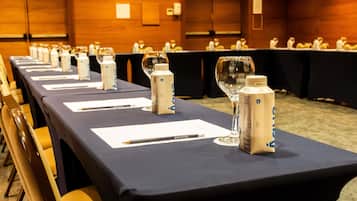 Una sala conferenze con lunghe tavolate, cartellini nominativi, bottiglie d'acqua e bicchieri.