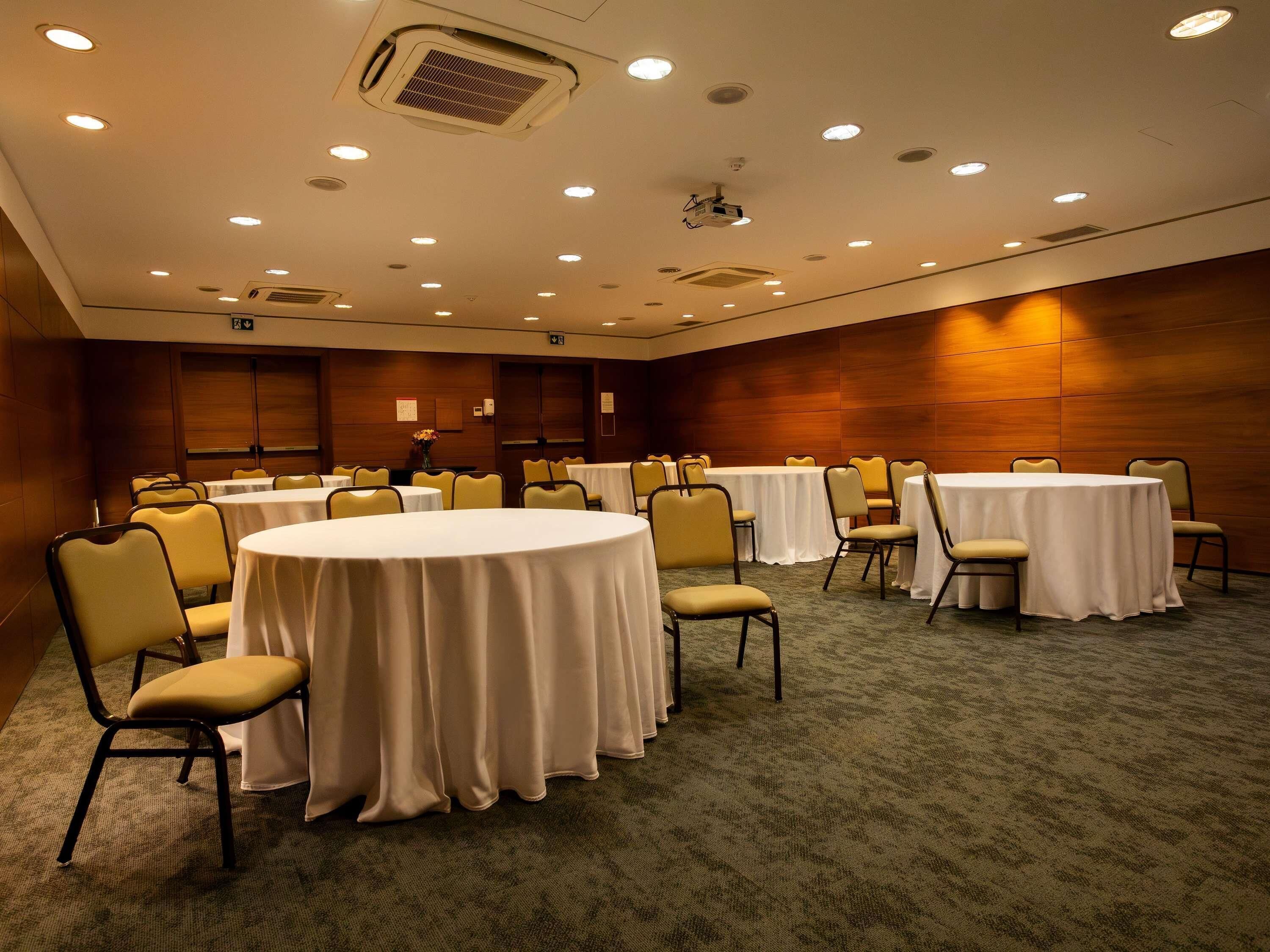 Un salón de conferencias con mesas redondas, sillas y suelo alfombrado.