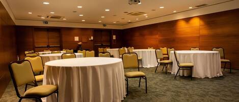Un salón de conferencias con mesas redondas, sillas y suelo alfombrado.