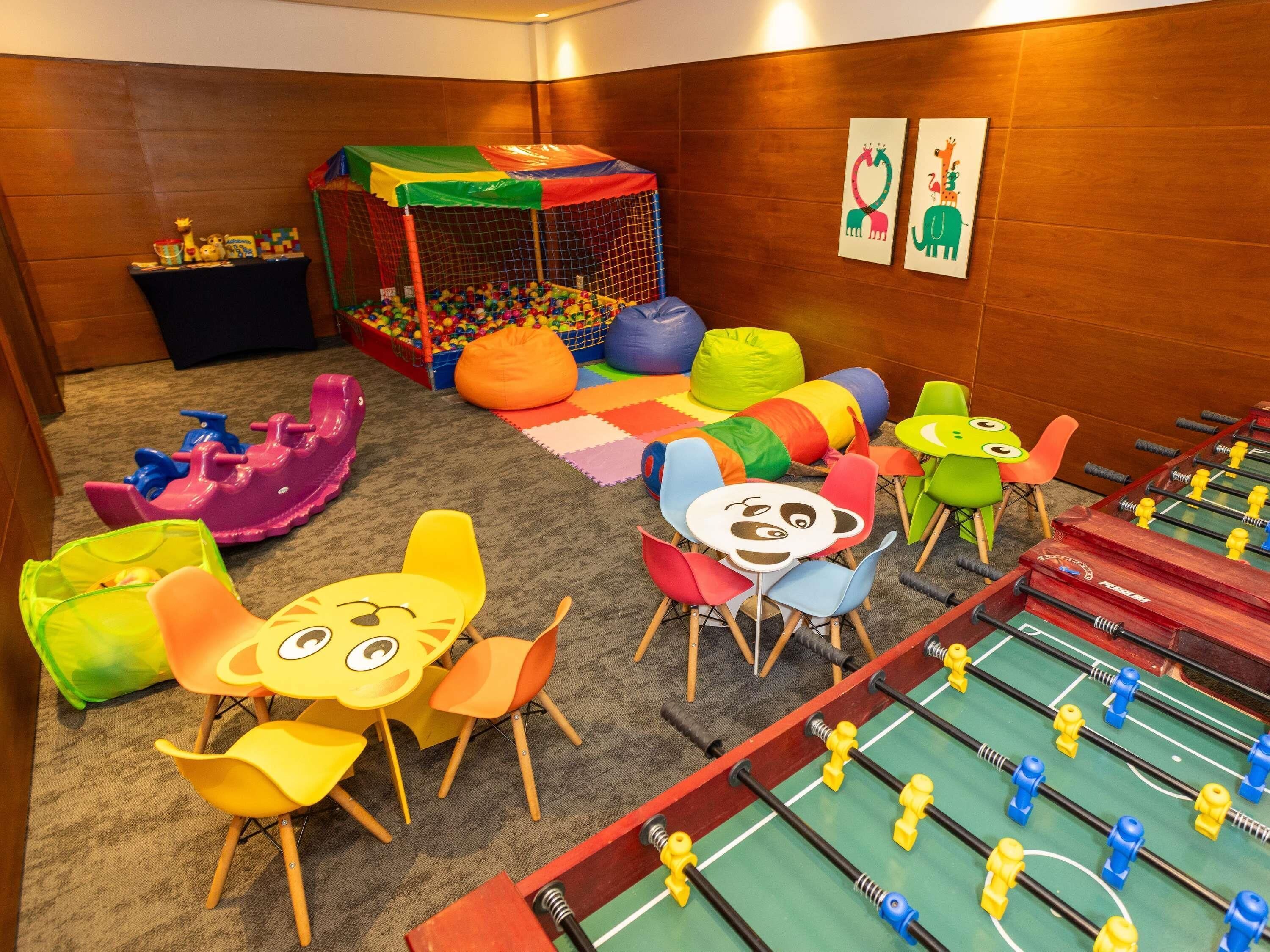 Een kinderspeelruimte met een bällebak, kleurrijke speeltoestellen en een tafelvoetbaltafel.