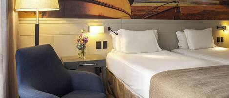 A hotel room with a bed, a chair, a desk, and a wall mural of a boat on the sea.