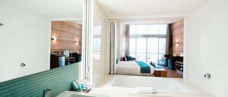 Une chambre d’hôtel moderne dotée d’un grand lit, d’une salle de bain séparée avec baignoire, d’un bureau et offrant une vue sur la ville grâce à de grandes fenêtres.