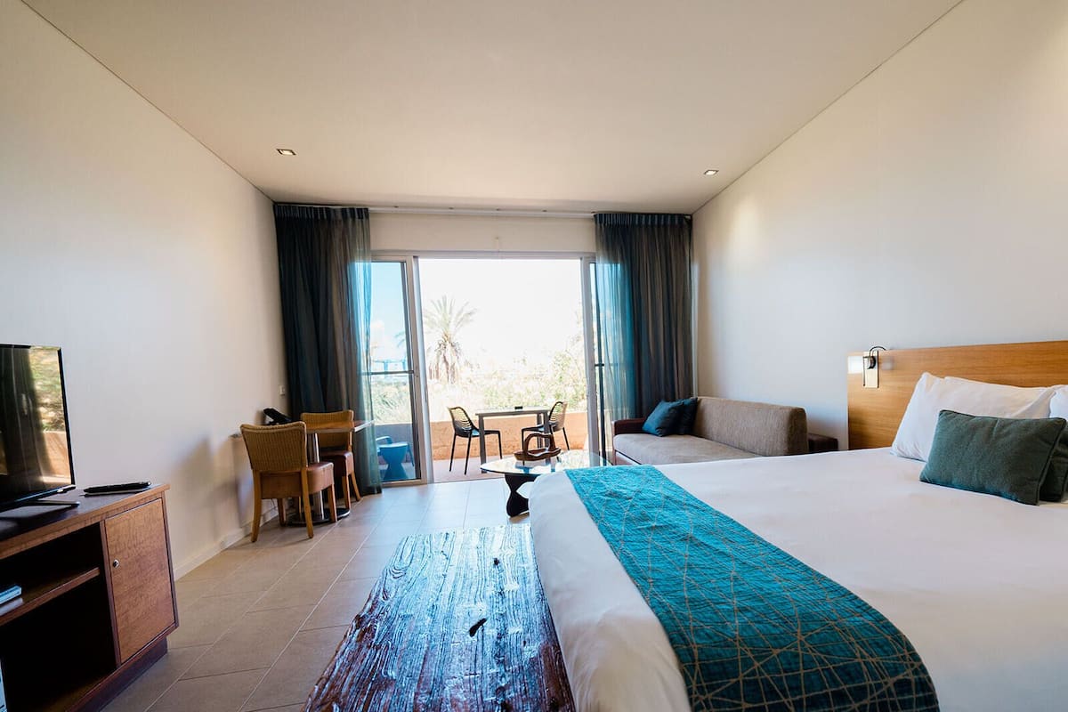 Een hotelkamer met een bed, een bureau, een stoel, een televisie en een balkon met gordijnen.