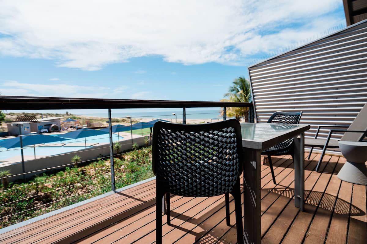 Een terras met een tafel en stoelen, met uitzicht op een zwembad en strand.