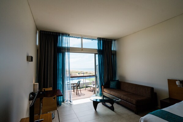 Una habitación de hotel con balcón, sofá, cama, escritorio y silla.