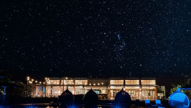 A modern hotel with a pool, starry night sky, and illuminated structures.