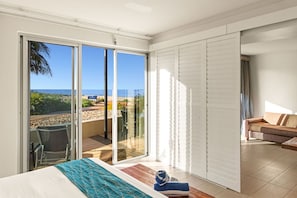 A bedroom with a bed, a view of the ocean through sliding glass doors, a balcony with a chair, and a sofa. - Mantarays Ningaloo Beach Resort (Exmouth)