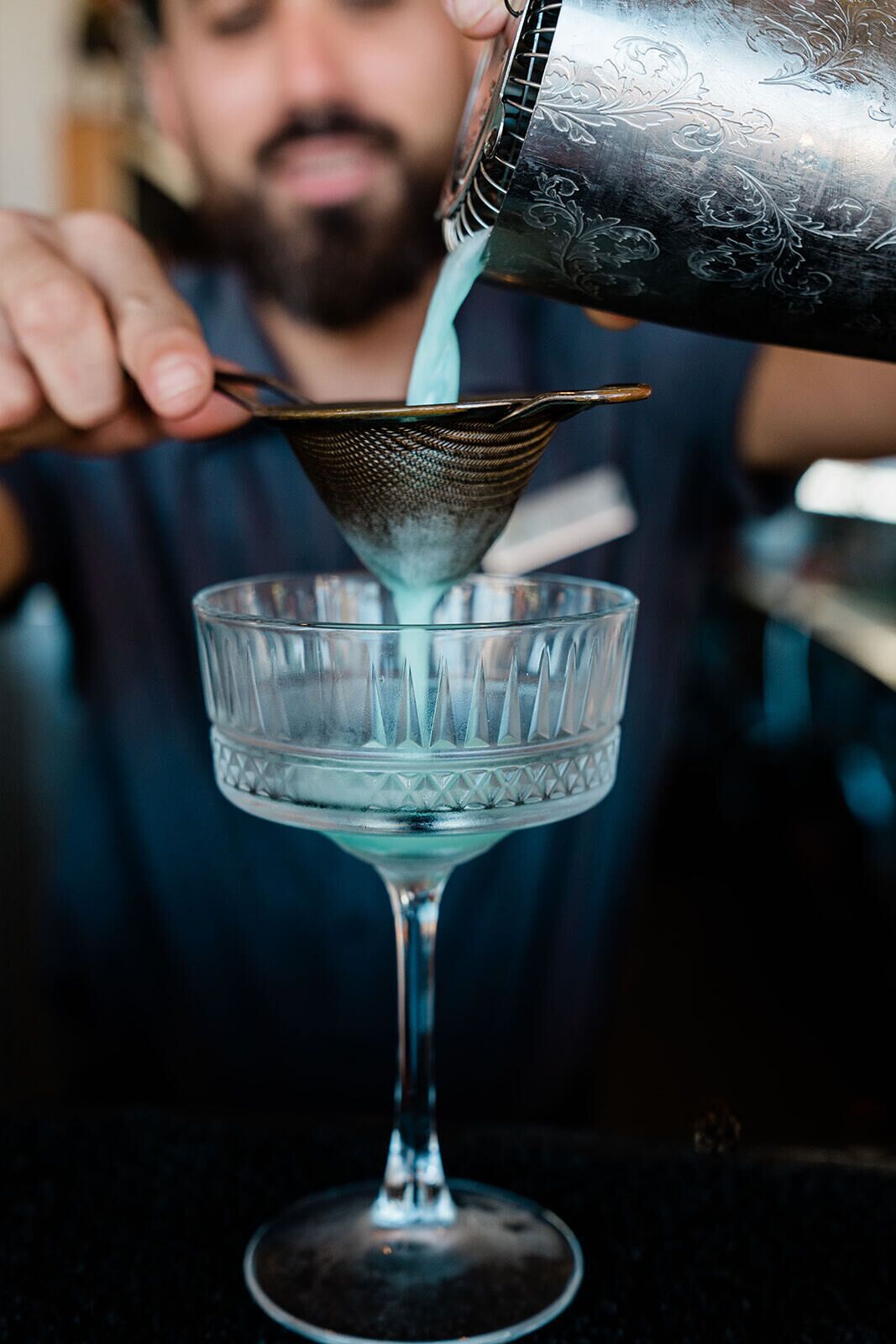 Une personne verse un liquide transparent dans un verre à l’aide d’une passoire en métal.
