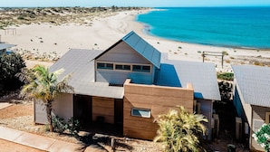 A coastal property with a beach view, featuring a modern house with a sloped roof and a small patio area.