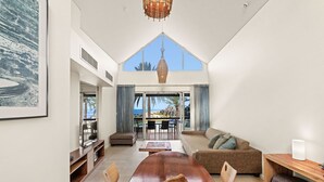A spacious living room with a large wooden dining table, comfortable seating, a television, and a view of the outdoors through large windows.
